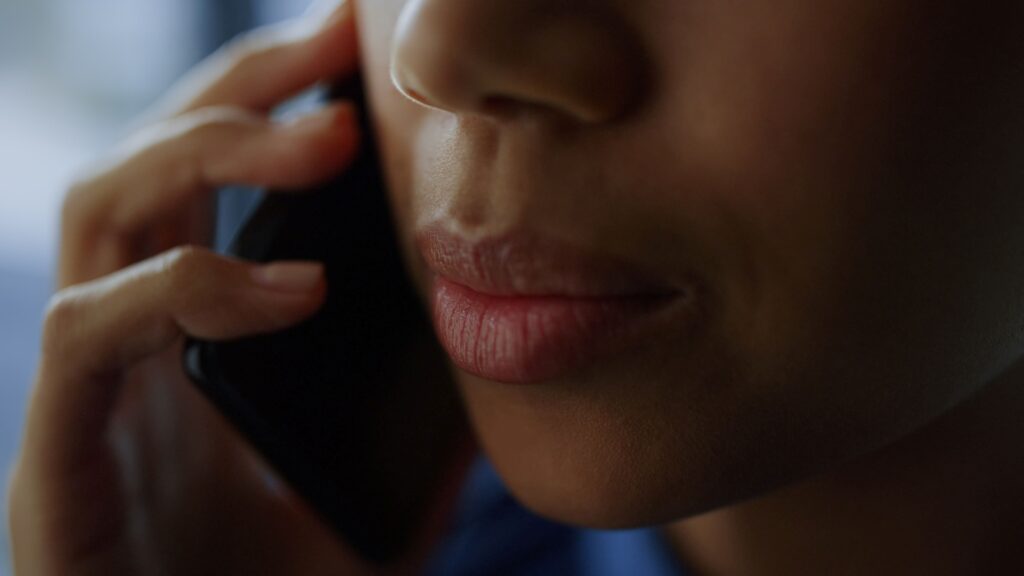 A close-up of a person holding a smartphone near their face while speaking during a phone call.
