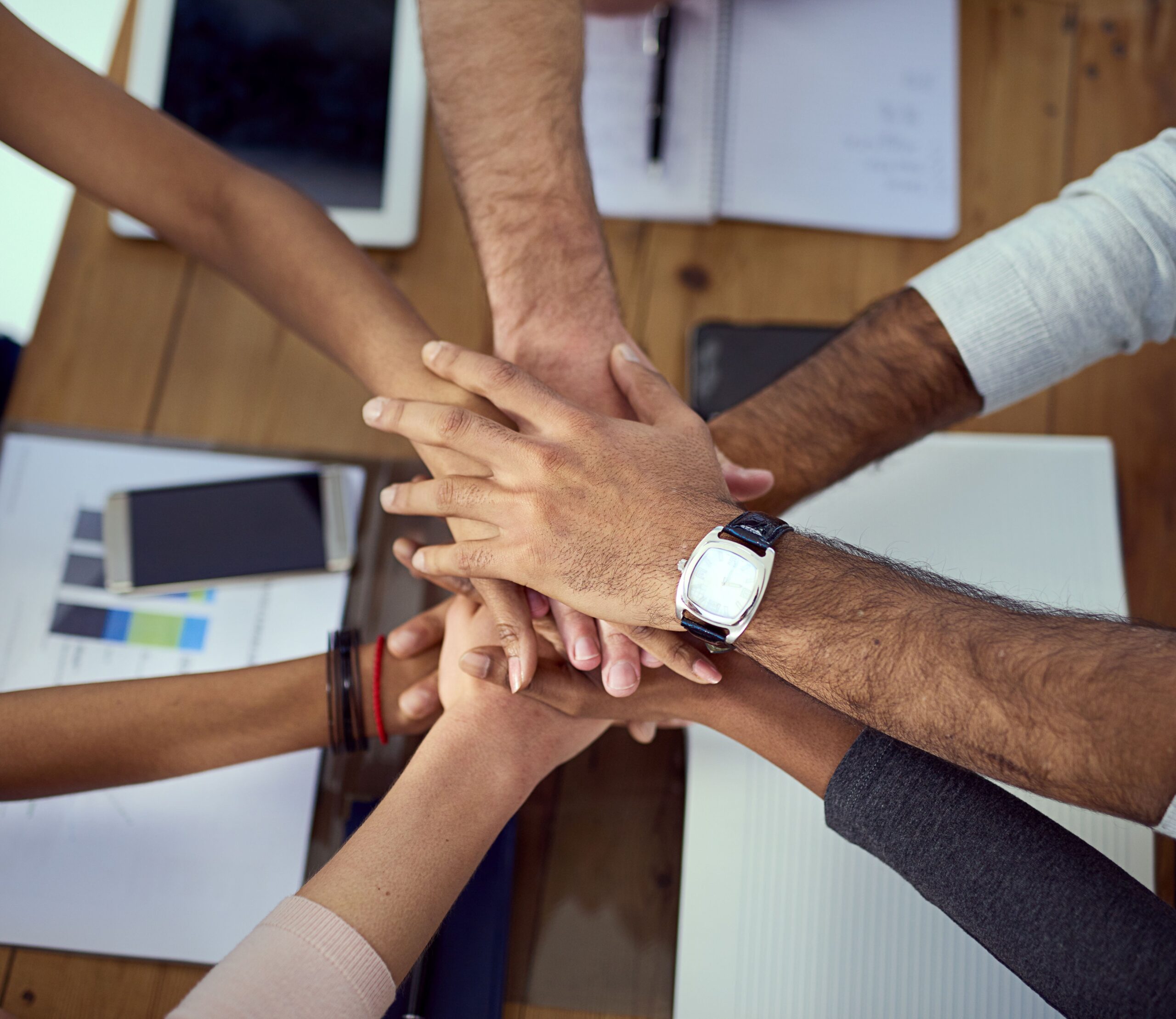 Multiple hands stacked together over a wooden table, symbolizing unity and teamwork.